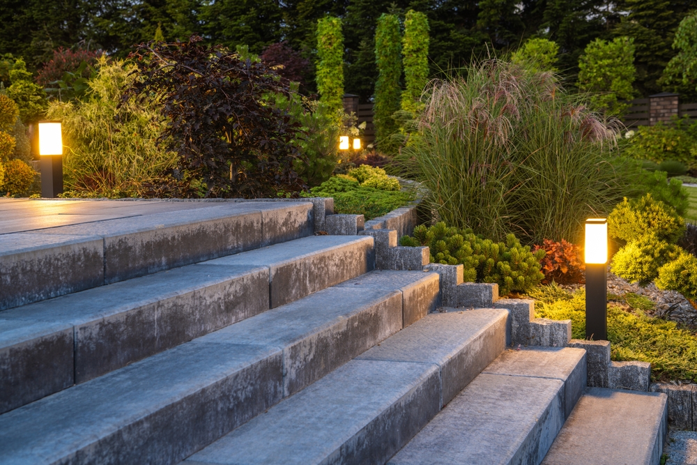 Closeup of concrete stairs in beautifully landscaped backyard garden planted with various shrubs and bushed and decorated with outdoor garden lights