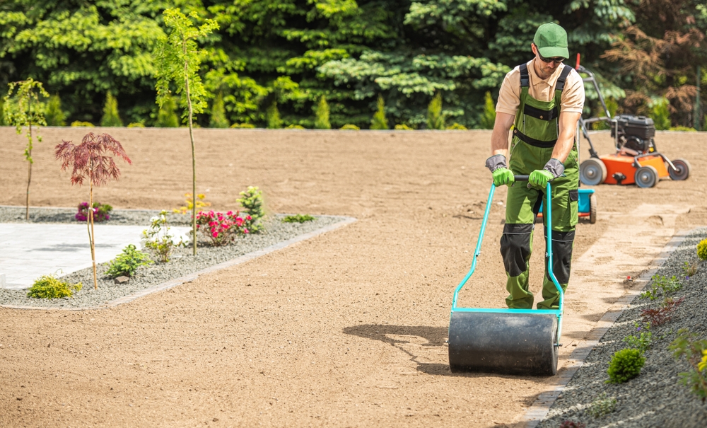 Professional Caucasian landscaper preparing backyard garden soil for grass seeding using compactor